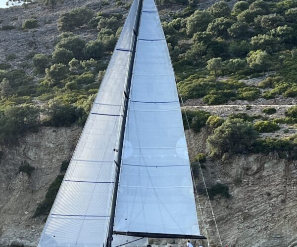 Elegant high-end sailing yacht with expansive sails cruising by cliffs.