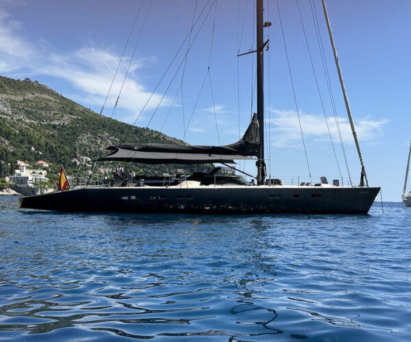 Elegant black sailing yacht moored in a picturesque coastal setting.