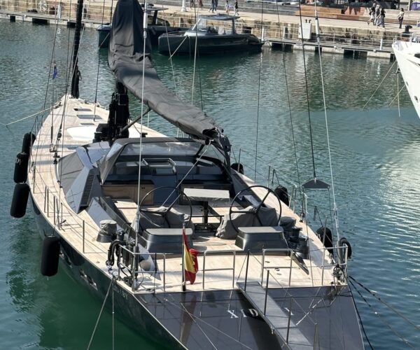 Elegant black sailing yacht docked in a marina with palm trees and cityscape in the background.